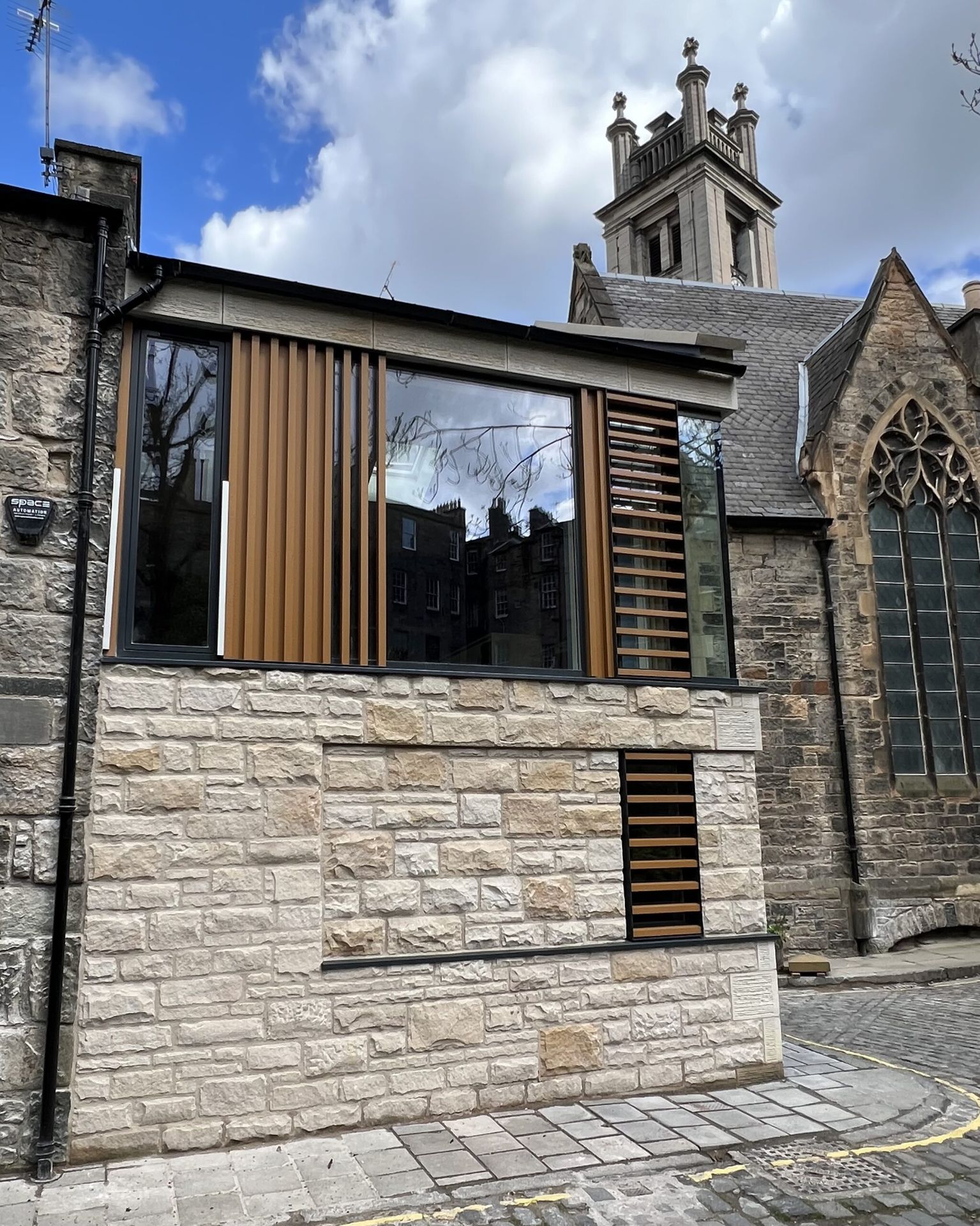 Contemporary stone masonry extension with wooden detailing on historic church building in Edinburgh.